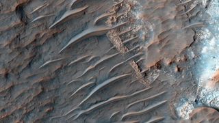 view of mars from orbit showing reddish-brown sand dunes rippling across a rocky surface