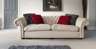 neutral living room wit a beige Chesterfield button-back sofa pulled out from the wall