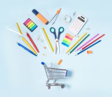 various school supplies pointing toward a miniature shopping cart