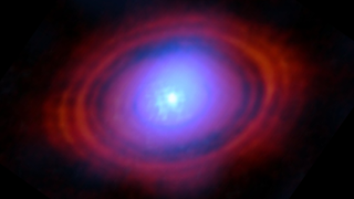 A slightly blurry blue orb in the center of the image is surrounded by a gradient disk of purple, and then red, hazes. The structure is seen against a black background.
