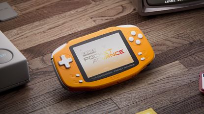 Render of upcoming Konkr Pocket Advance handheld on woodgrain surface with PS1 corner on left and edge of Famicom controller out of view on right.