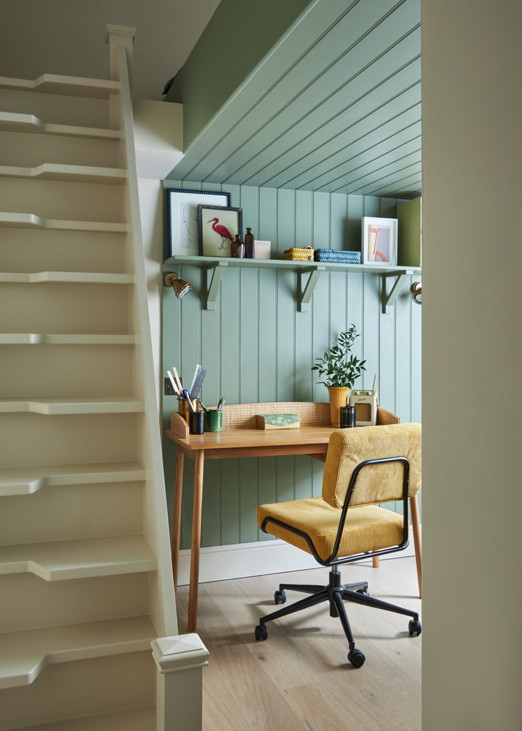 An office with sage green with witches stairs, a timber desk and yellow office chair, timber panelled walls and ceiling, timber floors, and floating shelf