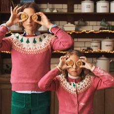 Woman and girl holding orange slices in front of their eyes wearing Boden Christmas jumpers