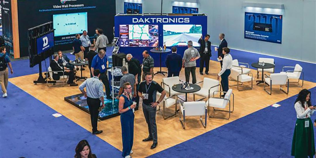 The Daktronics booth with chairs, people and multiple displays at InfoComm.