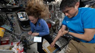 A man and a woman move small plastic tubes around on a table in microgravity