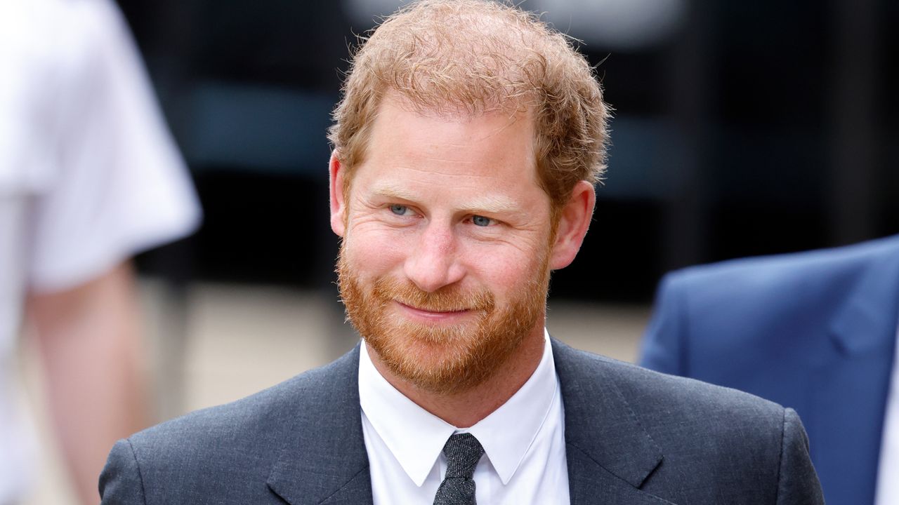 Prince Harry wears a suit and tie and has short red hair and a beard