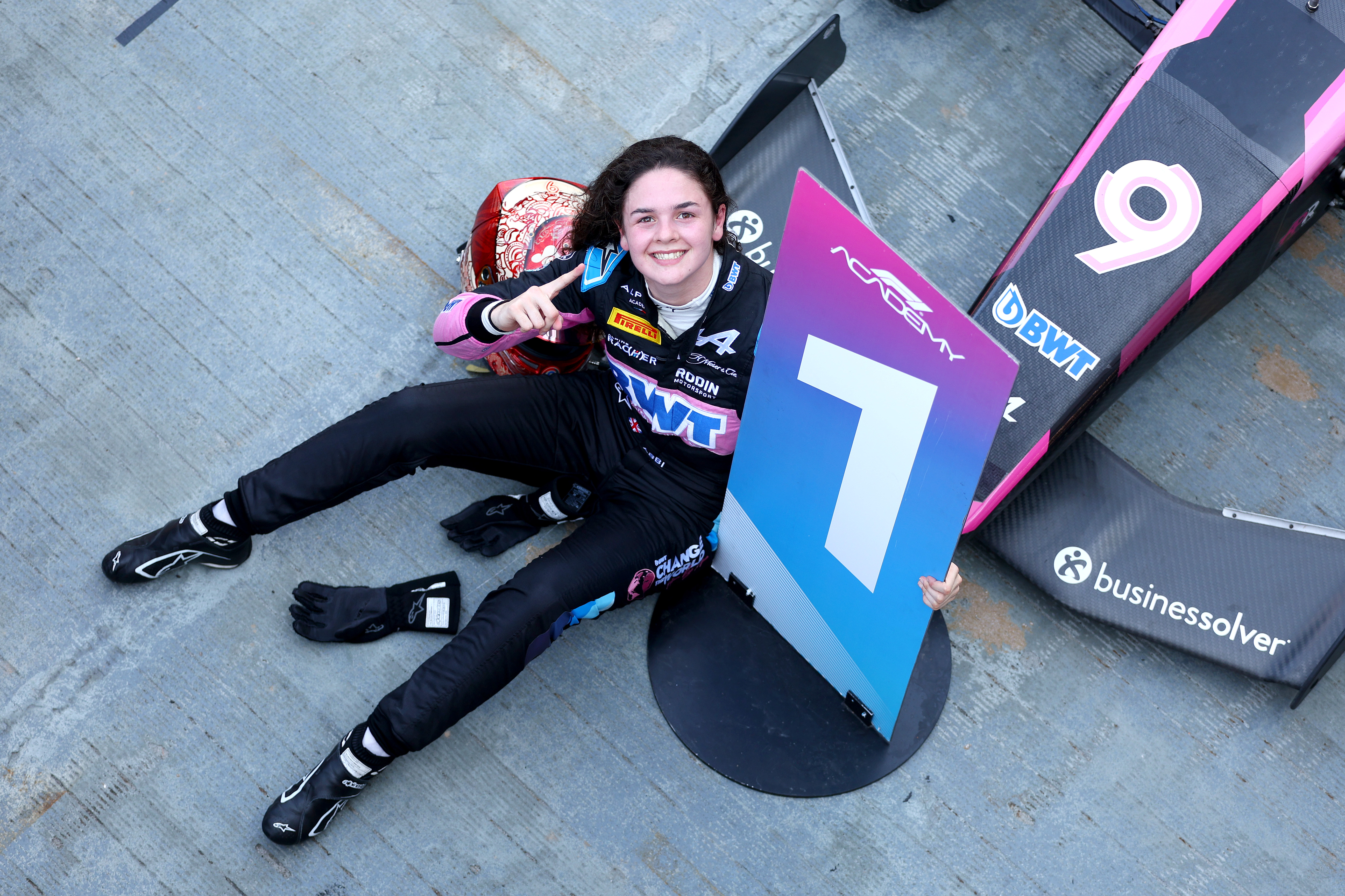 Girl in race suit holding a number one poster board