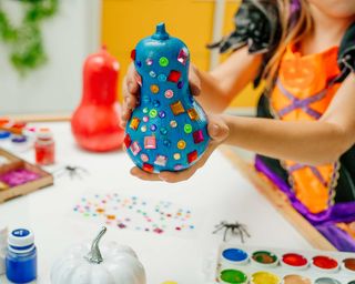 Child decorating colored painted pumpkins with shine stickers