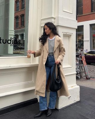 Kristin wears a trench, grey cardigan, blue jeans and black boots