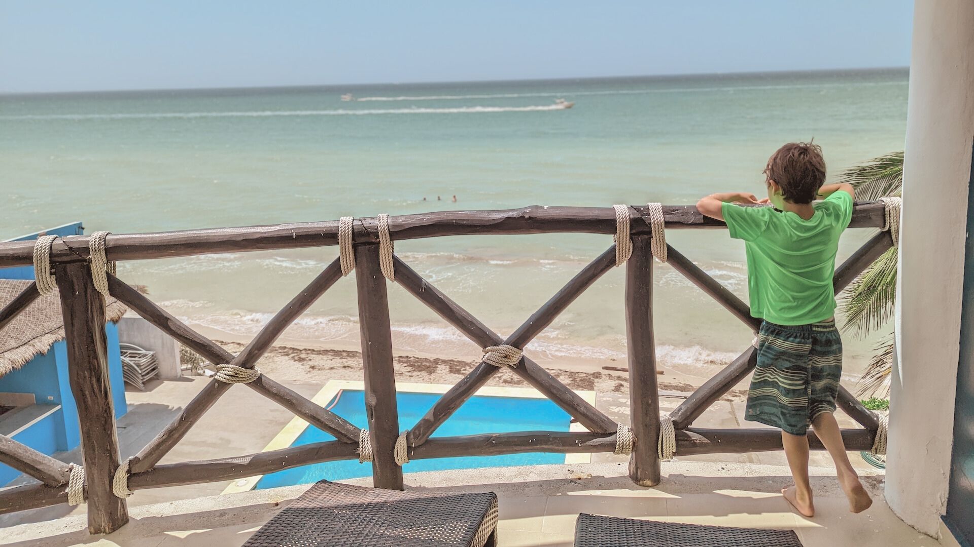 a young boy on a balcony looks out over a tropical beach