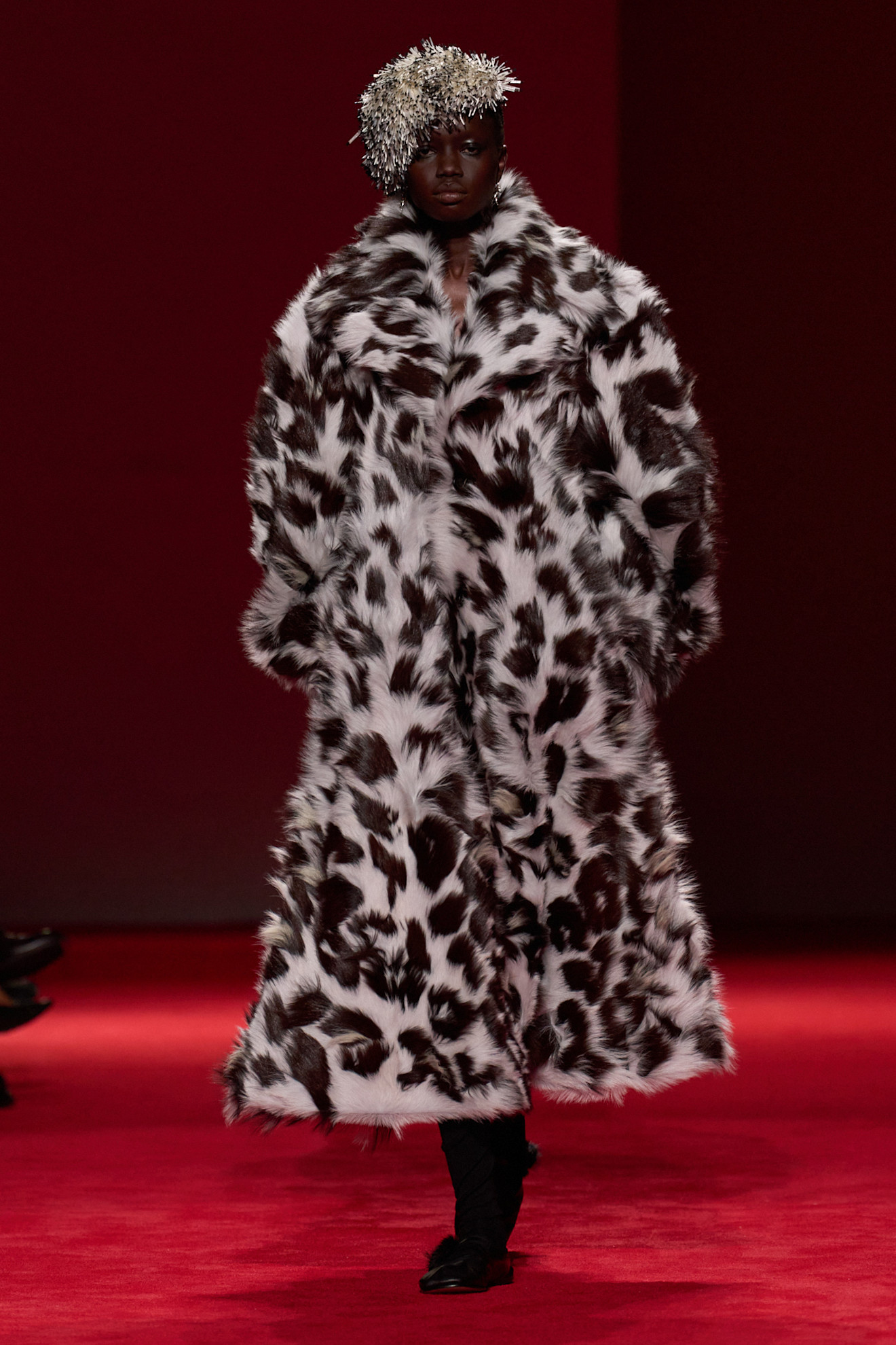A model walking in the Bottega Veneta F/W 26 show wearing a beaded hat and a leopard-print fringe coat.