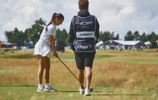 Female golfer ready to drive getting tips from her caddie