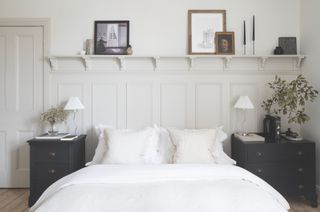 A white bedroom with a double bed and sentimental items displayed on a shelf above the bed