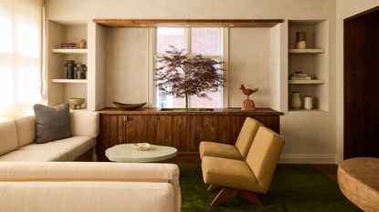 Living room with cream plaster walls, cream corner sofa, ochre armchairs, rough edged mint coffee table, wood sideboard and indoor tree planted inside