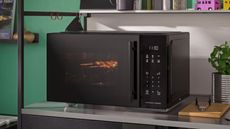 Black microwave on stainless steel shelf in green kitchen