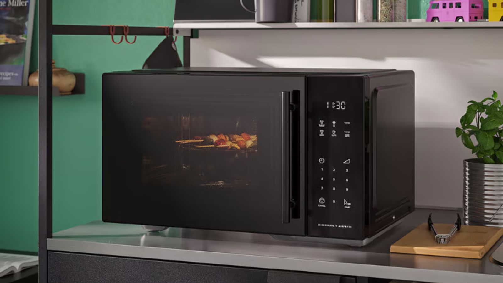 Black microwave on stainless steel shelf in green kitchen