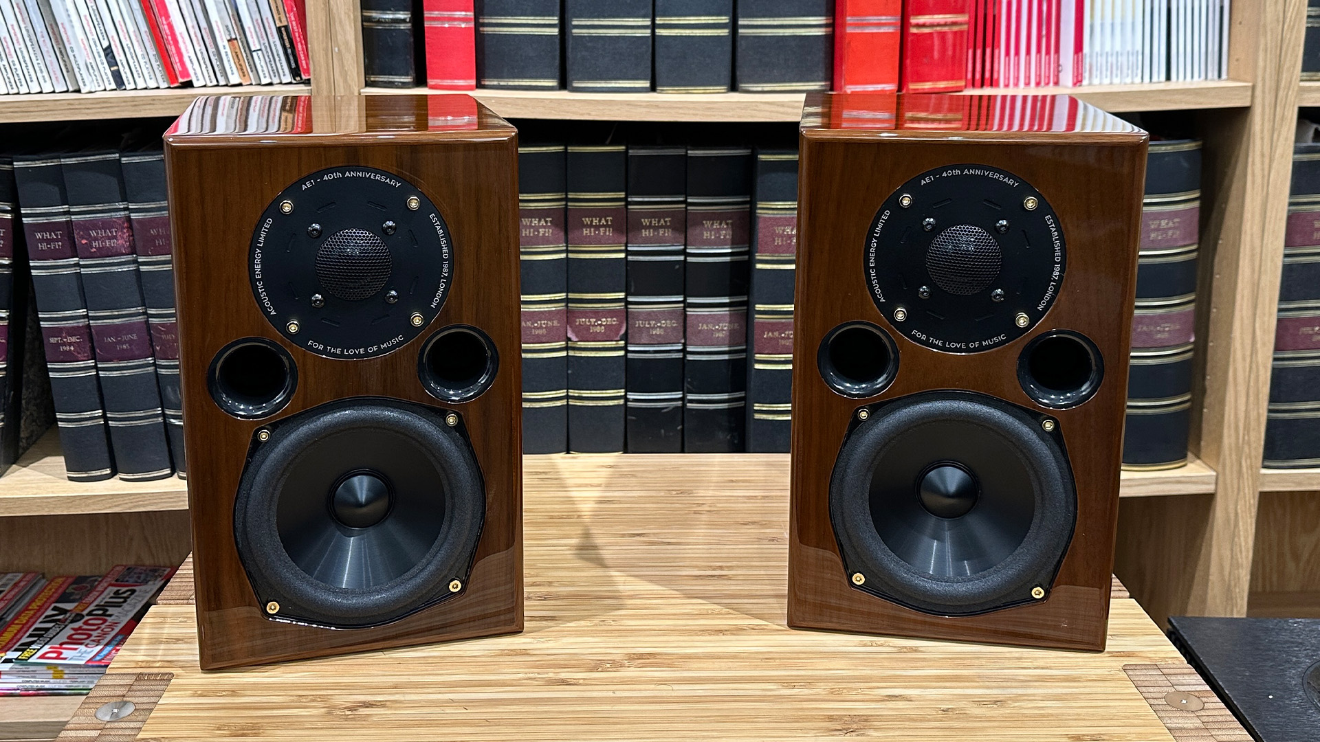 Acoustic Energy AE1 40th Anniversary standmount speakers on wooden hi-fi rack in front of bookcase