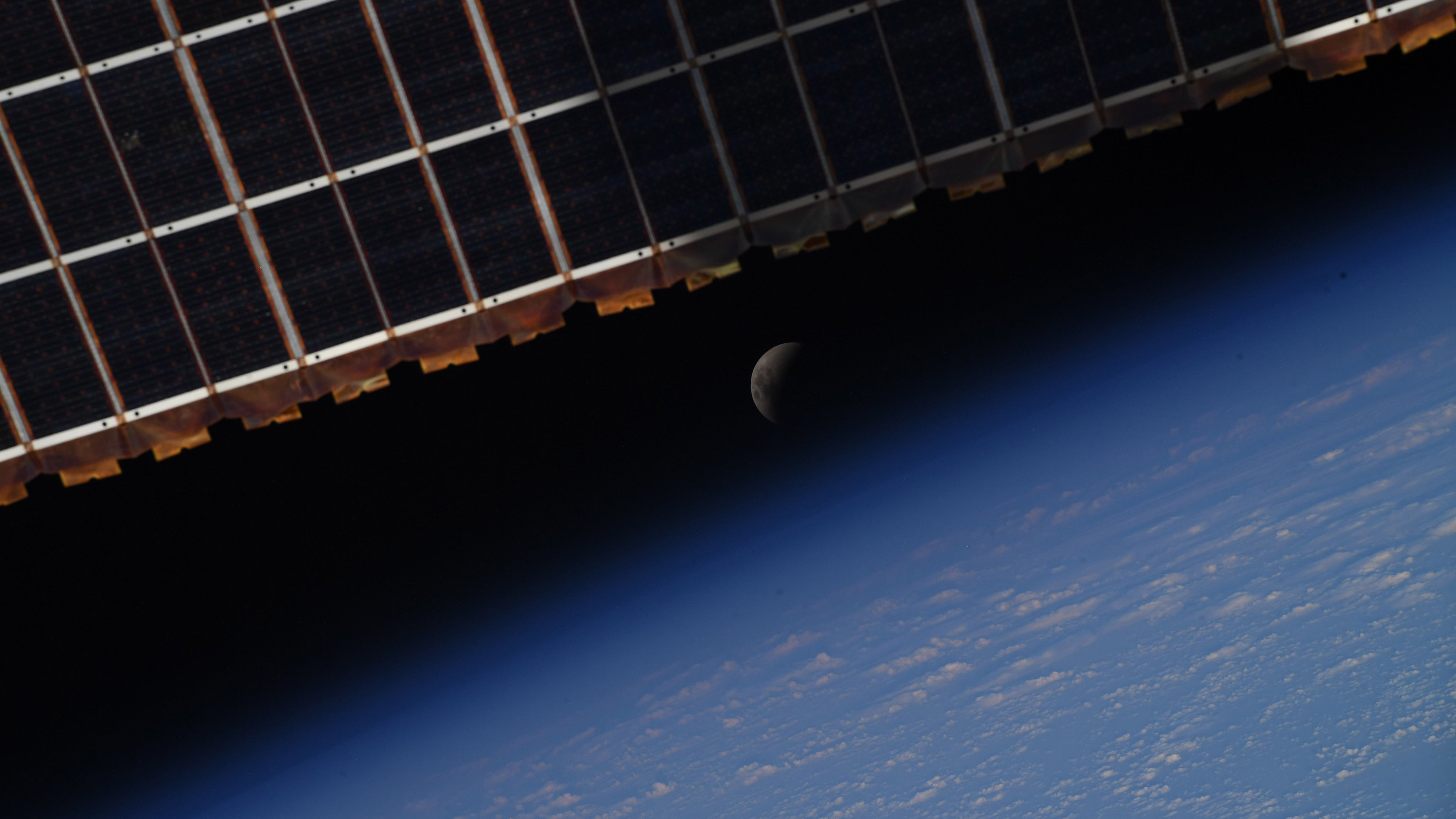 The eclipsed moon peeking through the solar panels of the International Space Station