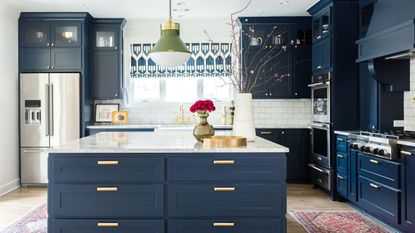 blue and white kitchen with patterned blinds and rugs, a green pendant light, and flowers in a vase on a large central island