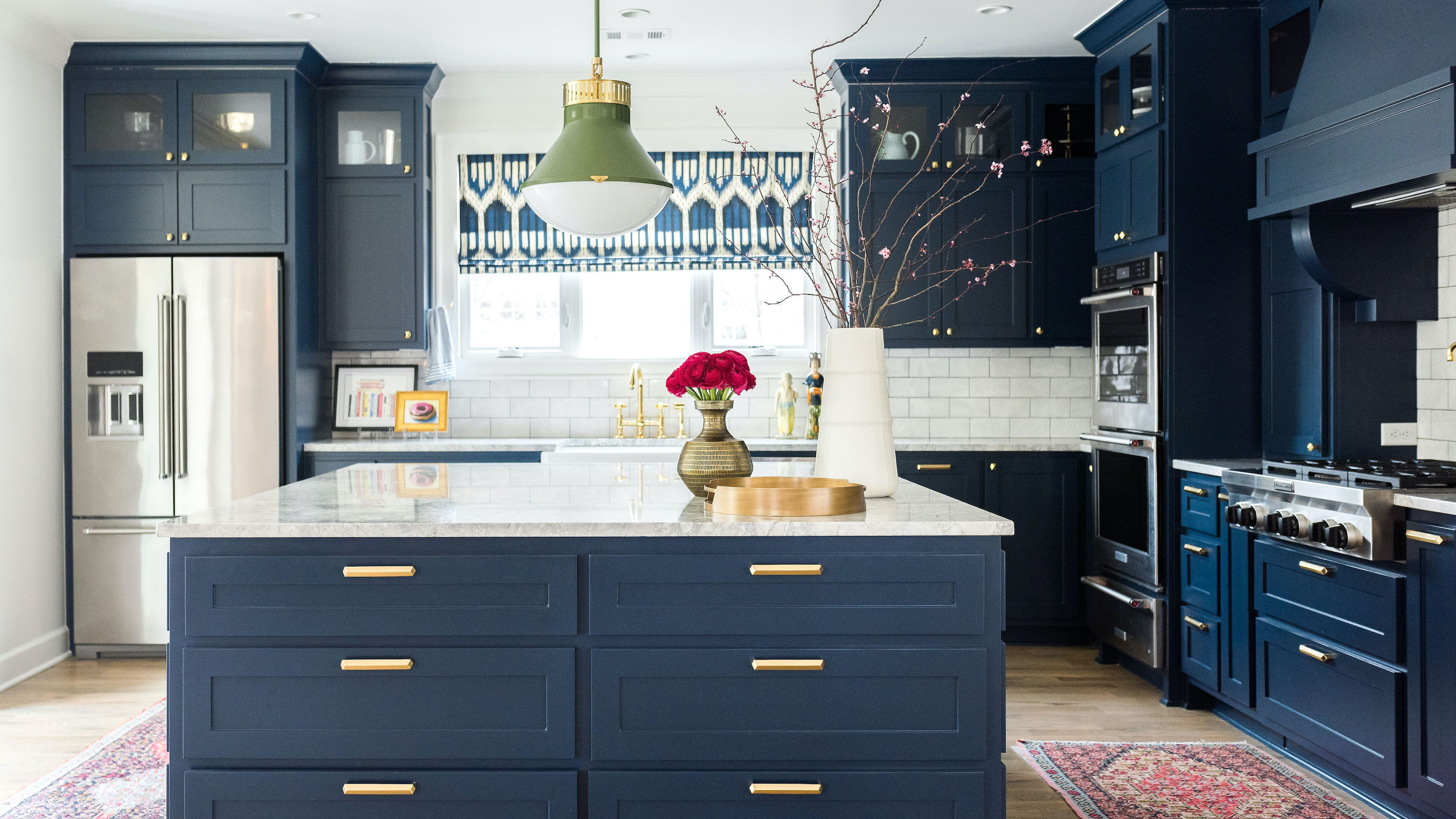 blue and white kitchen with patterned blinds and rugs, a green pendant light, and flowers in a vase on a large central island