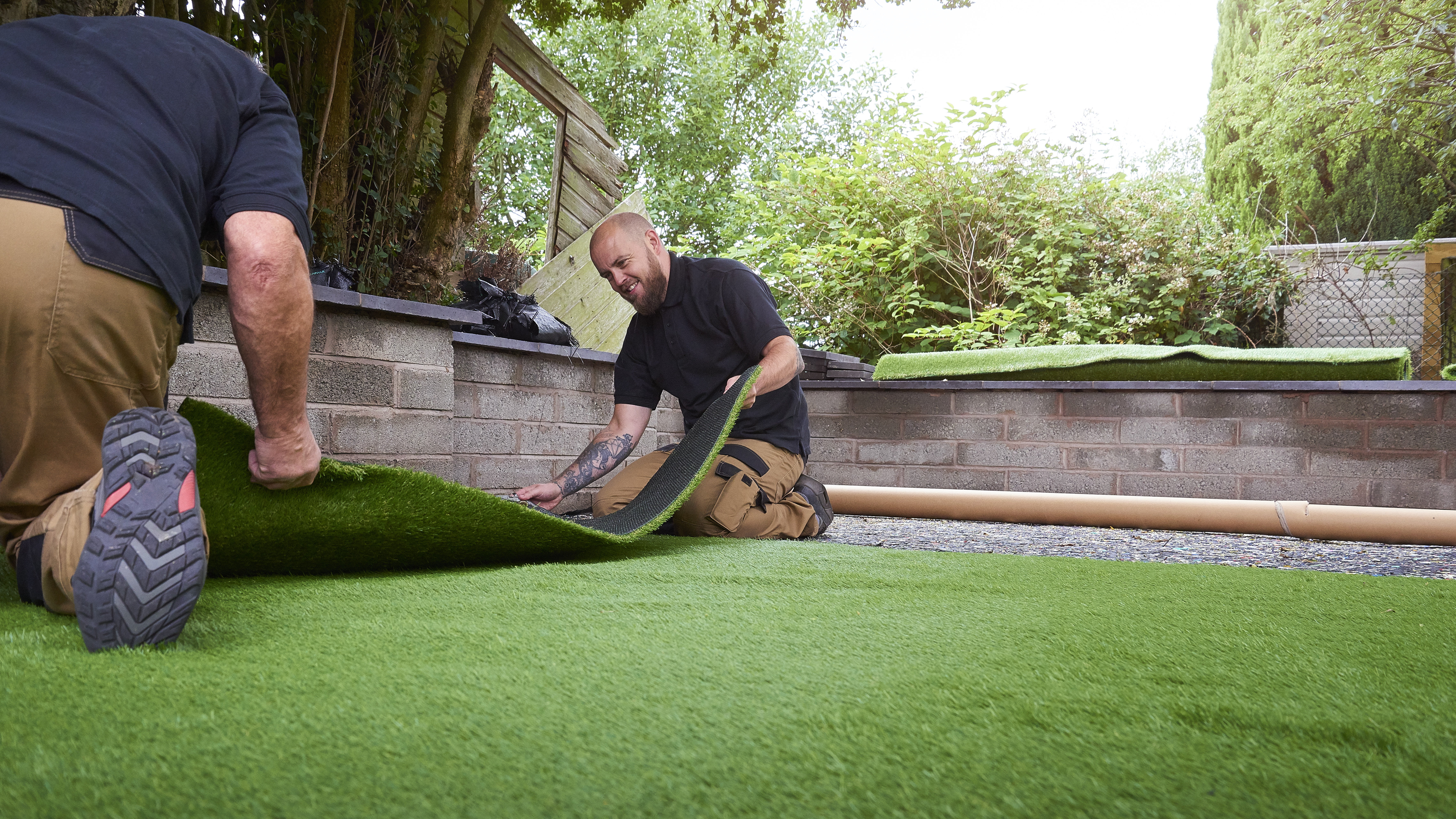 Two men laying a roll of artificial turf in a back yard