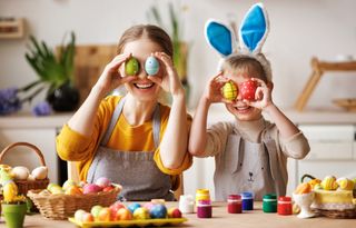 A mother and child sitting at a table covering their eyes with decorated easter eggs.