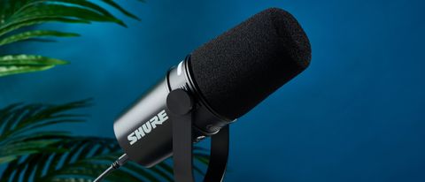 a black microphone with a desktop stand and a black muff is on top of a beige surface with a blue backdrop