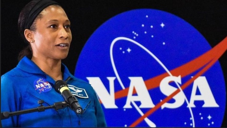 A woman standing in front of a microphone wearing a blue suit.