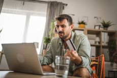 A man looking confused at his laptop holding a credit card