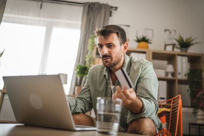 A man looking confused at his laptop holding a credit card