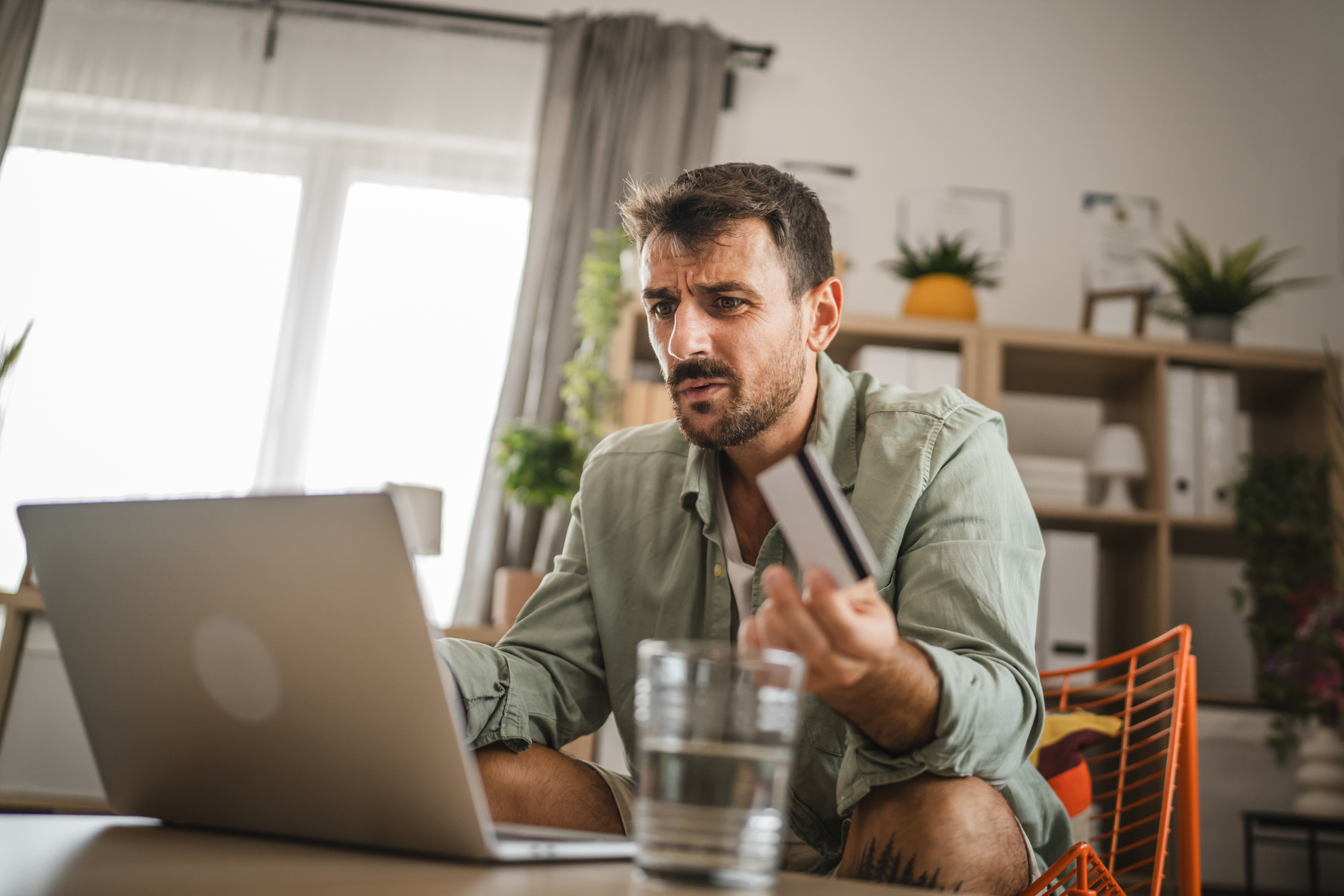 A man looking confused at his laptop holding a credit card
