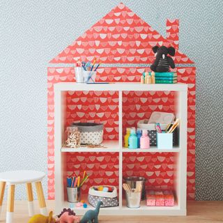 A square IKEA KALLAX unit used for toy storage with a wallpaper behind it creating a doll house look