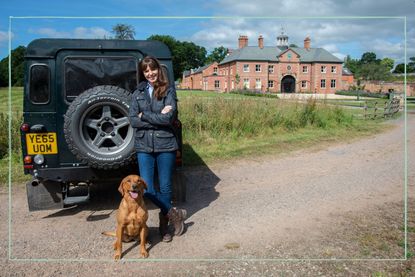 a medium shot of The Dog Academy expert Victoria Stillwell posing with a red labrador, next to a Land Rover jeep