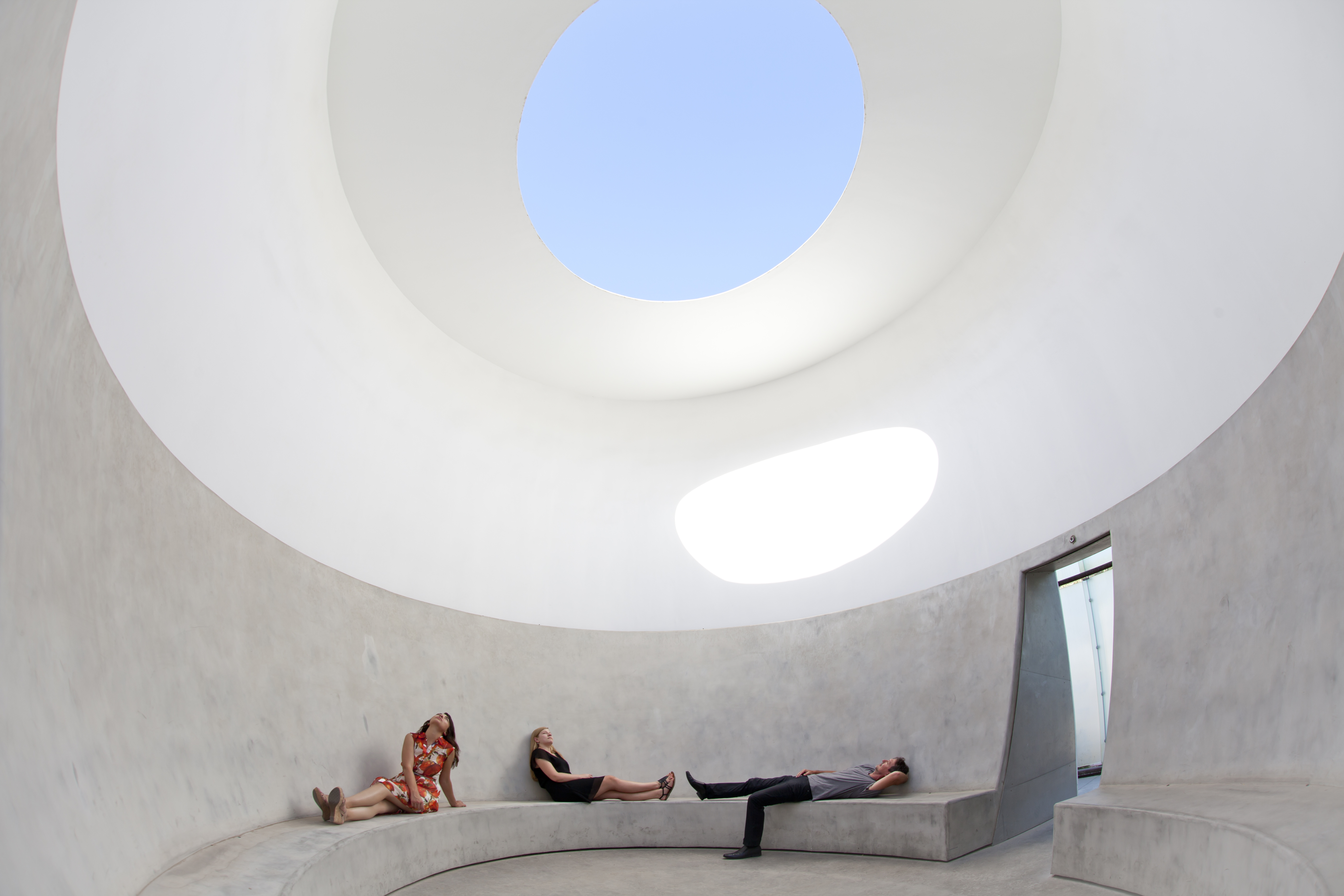 A pantheon-like architectural installation in cement, placed inside a museum, allows visitors to recline indoors while staring at the sky through a hole in the ceiling.