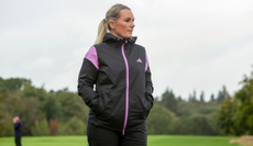 A golfer wears the adidas Women's Rain.RDY Golf Jacket in black and purple