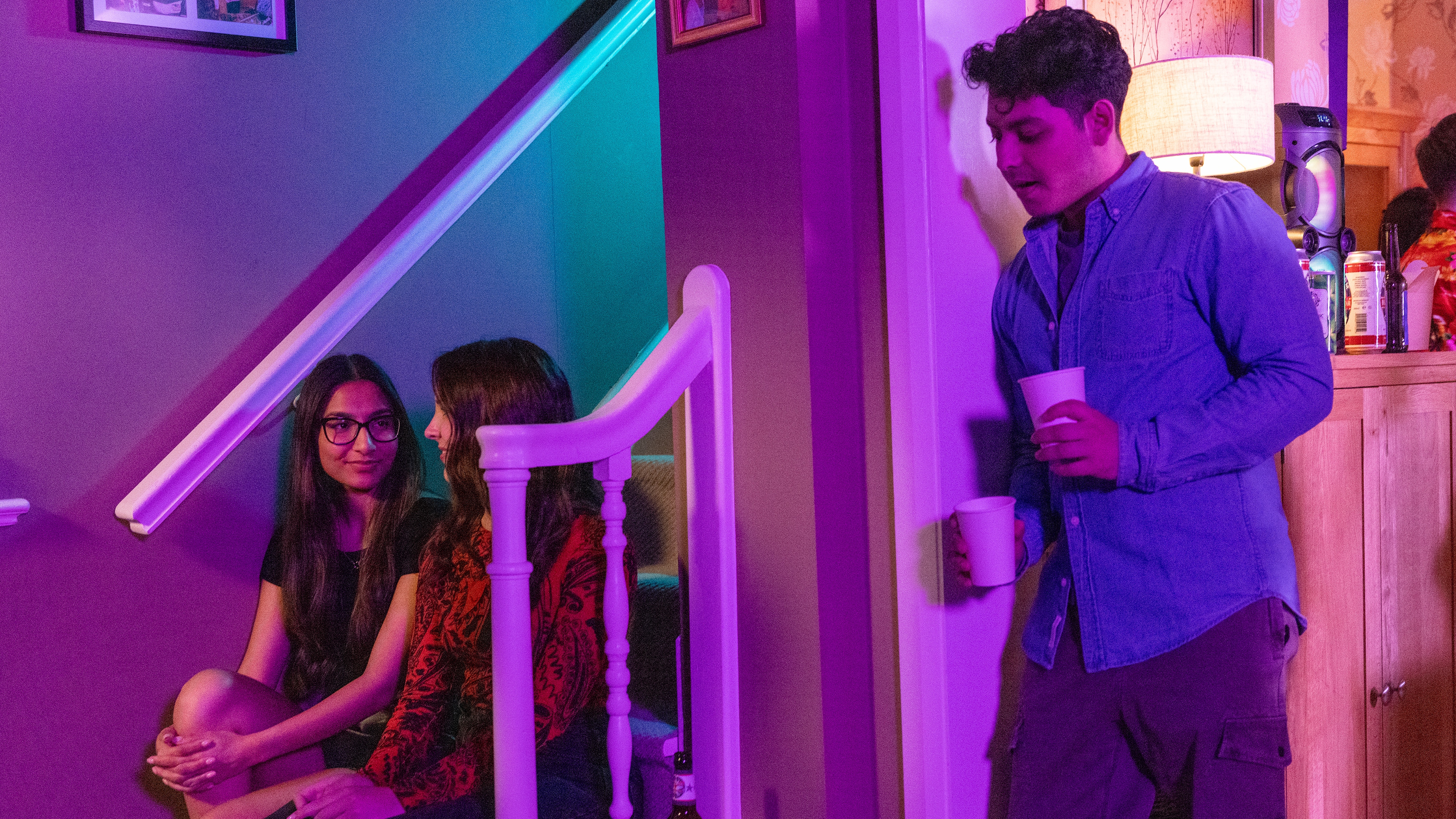 Aadi listens to Asha and Amy's conversation behind a wall.