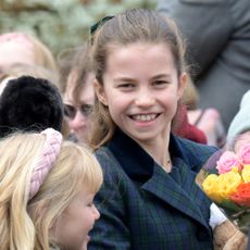 Princess Charlotte wearing a green plaid coat smiling at the camera amid a crowd of people