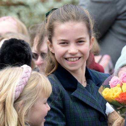 Princess Charlotte wearing a green plaid coat smiling at the camera amid a crowd of people