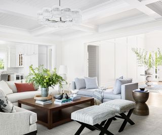 living room with white walls open plan to kitchen with white and gray sofas and footstools