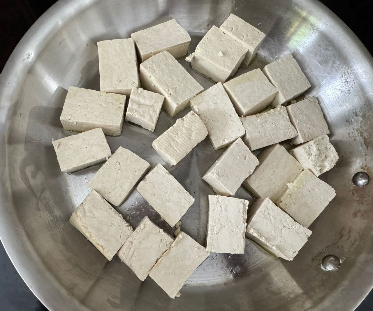 Uncooked tofu chunks in a stainless steel frying pan.