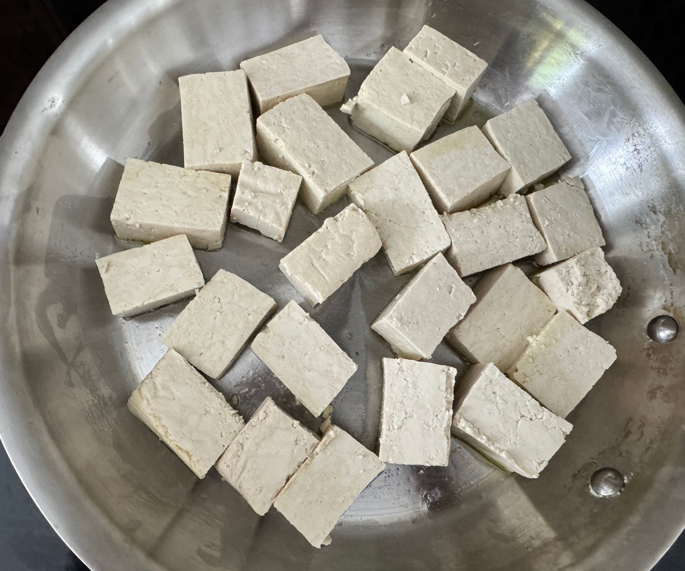 Uncooked tofu chunks in a stainless steel frying pan. 