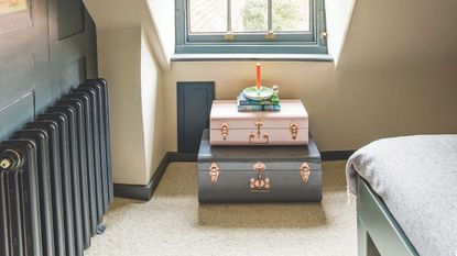 A black radiator in a dark blue and white attic bedroom with a stack of suitcases, orange candle, and corner of a blue bed with grey bedding