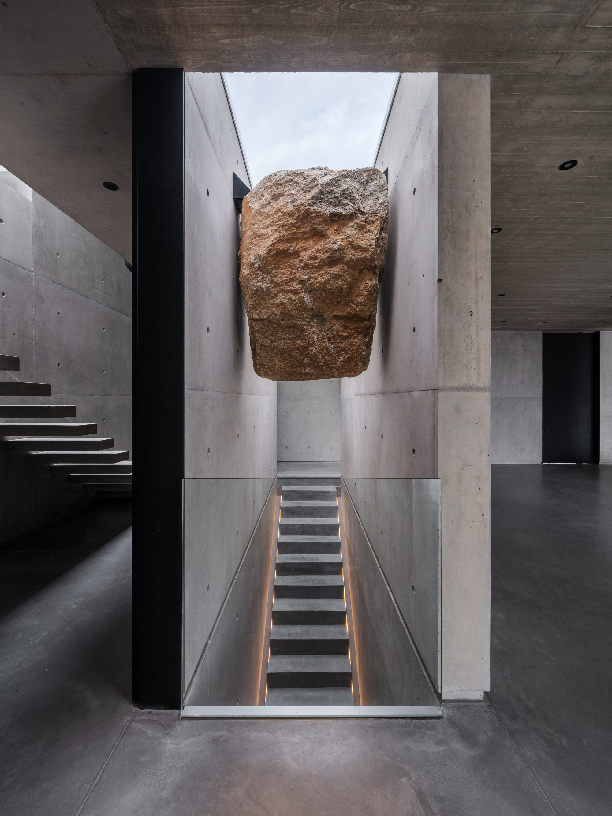 brutalist staircase with concrete walls and floors and ceiling, and a sculptural rock lodged in the stairwell