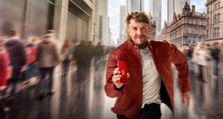 Roman Kemp running through a blurred cityscape with a phone in his hand, showing a Vodafone logo