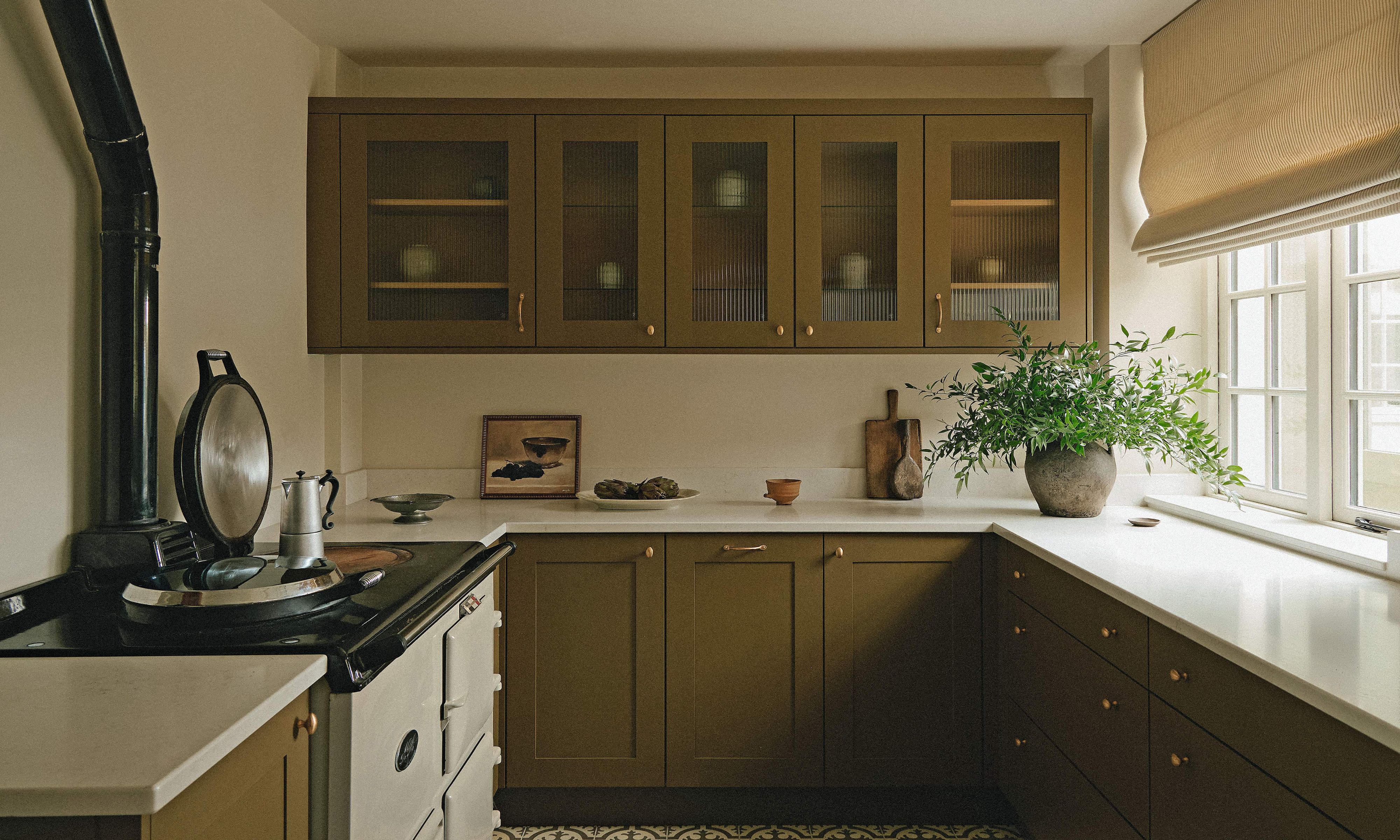 a small country kitchen with traditional AGA cooker, olive green cabinetry and neutral walls and decor