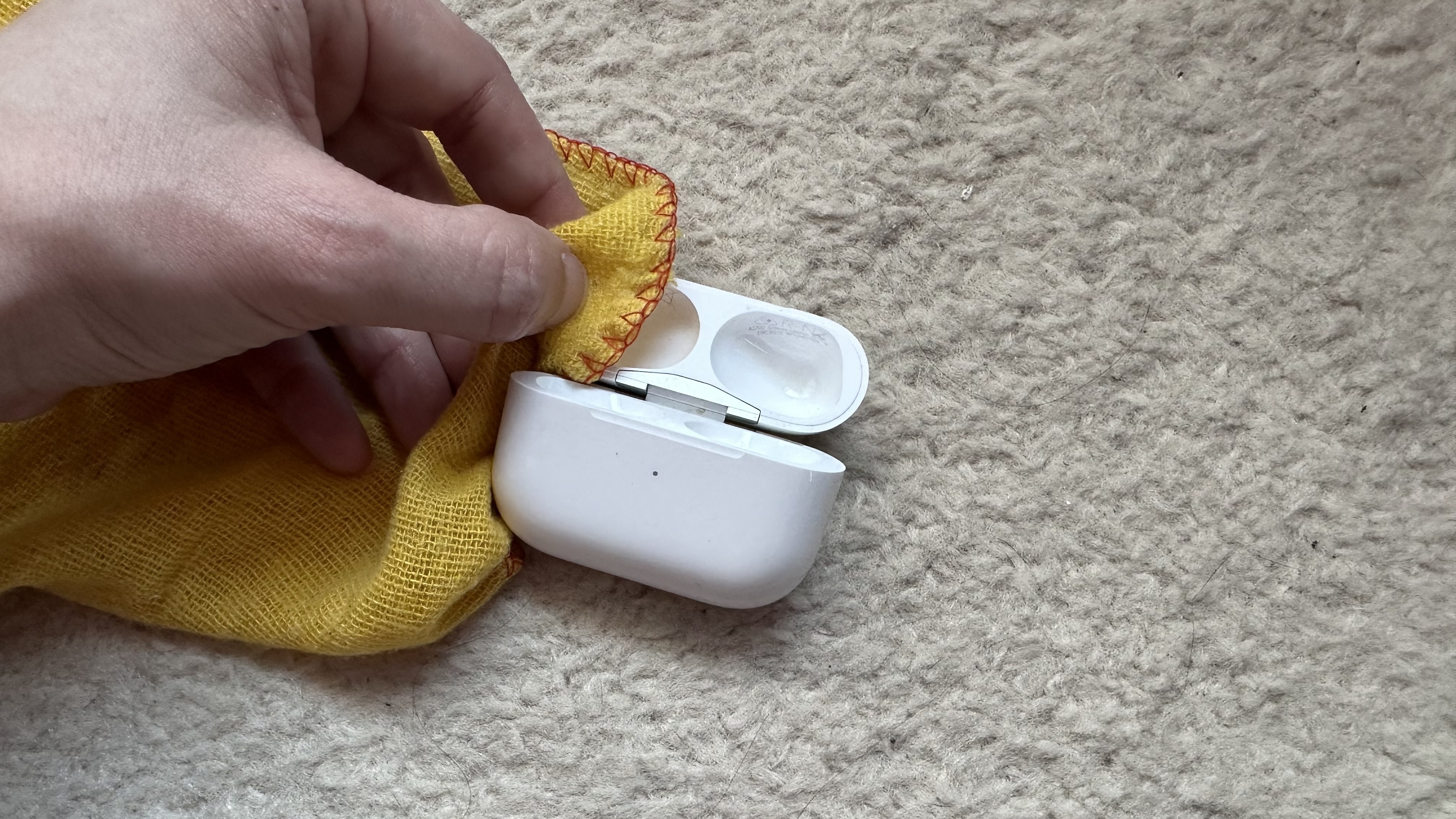 Someone cleaning an Apple AirPods Pro case with a yellow cloth.