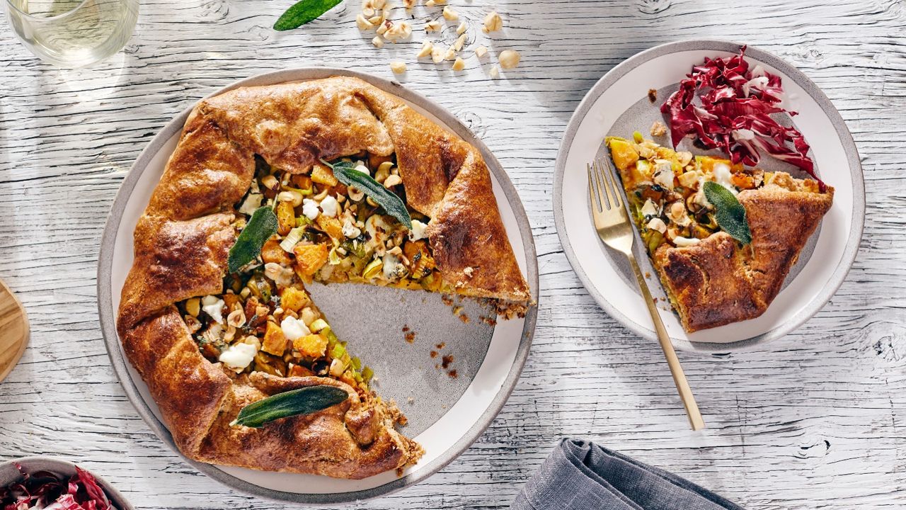 top down view of savory squash, leek, cheese, hazelnut galette open face pie with white wine on white wood table