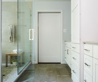 White wet room with glass shower door, blue walls and white cabinetry