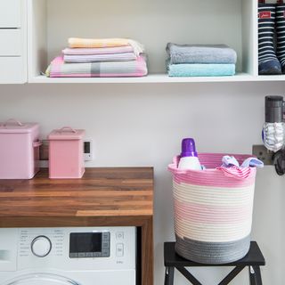 White utility room with towels stacked on open shelves and a basket of washing next to a washing machine