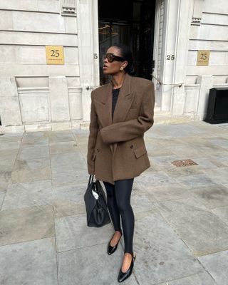 Influencer wears pointed toe flats, black leggings, a brown blazer, and a black tote bag.